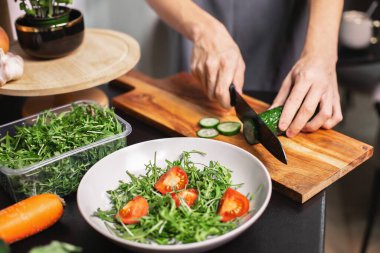 Mutfakta salatalık doğrayan mutlu genç çocuk taze sebze salatası hazırlıyor. Sağlıklı yaşam tarzı konsepti, otantik.