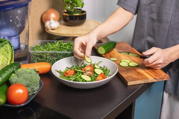 Mutfakta salatalık doğrayan mutlu genç çocuk taze sebze salatası hazırlıyor. Sağlıklı yaşam tarzı konsepti, otantik.