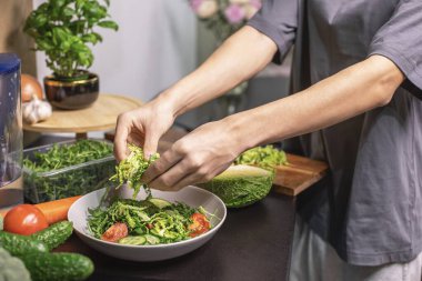 Genç çocuk taze sebze salatası hazırlıyor roka, salatalık ve domates mutfakta, sağlıklı yaşam tarzı ve çiğ gıda konsepti.