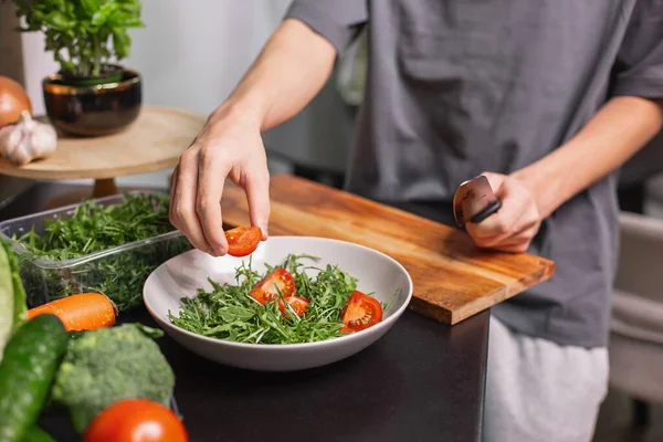 Genç çocuk taze sebze salatası hazırlıyor roka, salatalık ve domates mutfakta, sağlıklı yaşam tarzı ve çiğ gıda konsepti.
