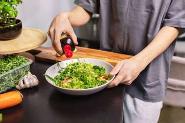 Genç çocuk mutfakta taze sebze salatası hazırlıyor ve giydiriyor, sağlıklı besleniyor, ev yemeği ve sağlık konsepti yapıyor..