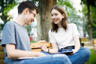 Okul arkadaşları okul bahçesinde bankta oturup konuşuyor.