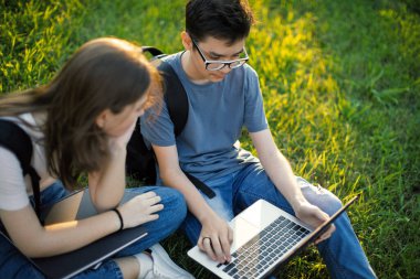 Okul arkadaşları okul bahçesinde çimlerin üzerinde oturarak konuşuyor.