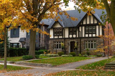 Bahçesinde sonbahar yaprakları olan küçük taş bir evin ön tarafı..