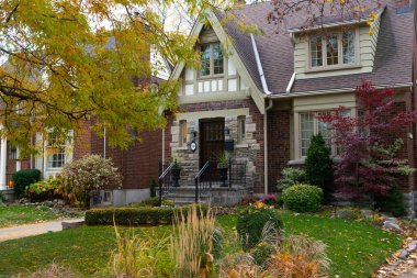 Bahçesinde sonbahar yaprakları olan küçük taş bir evin ön tarafı..