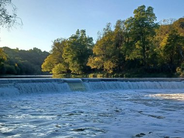 Akşam güneşi Humber Nehri somon merdivenini aydınlatıyor. İnsanlar nehir boyunca toplanıp akan suyu seyrediyorlar..