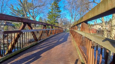 Culham Trail Köprüsü, güneşli bir günde çevresindeki ağaçları ve yapıyı yansıtan sakin bir su yolu boyunca uzanır..