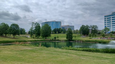 Charlotte, NC, ABD - 30 Nisan 2025: Modern ofis binaları yeşil çimenlerin, ağaçların ve Ballantyne Corporate Park 'ta bulutlu bir gökyüzünün altında bir yürüyüş yolunun ortasında duruyor.