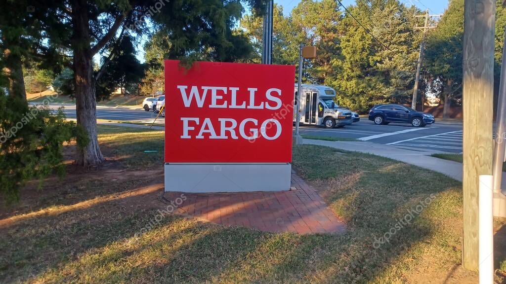 Charlotte, NC, USA - October 10, 2025: Large red Wells Fargo sign stands near a road and trees on a sunny autumn afternoon