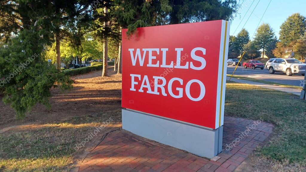 Charlotte, NC, USA - October 10, 2025: Large red Wells Fargo sign stands near a road and trees on a sunny autumn afternoon