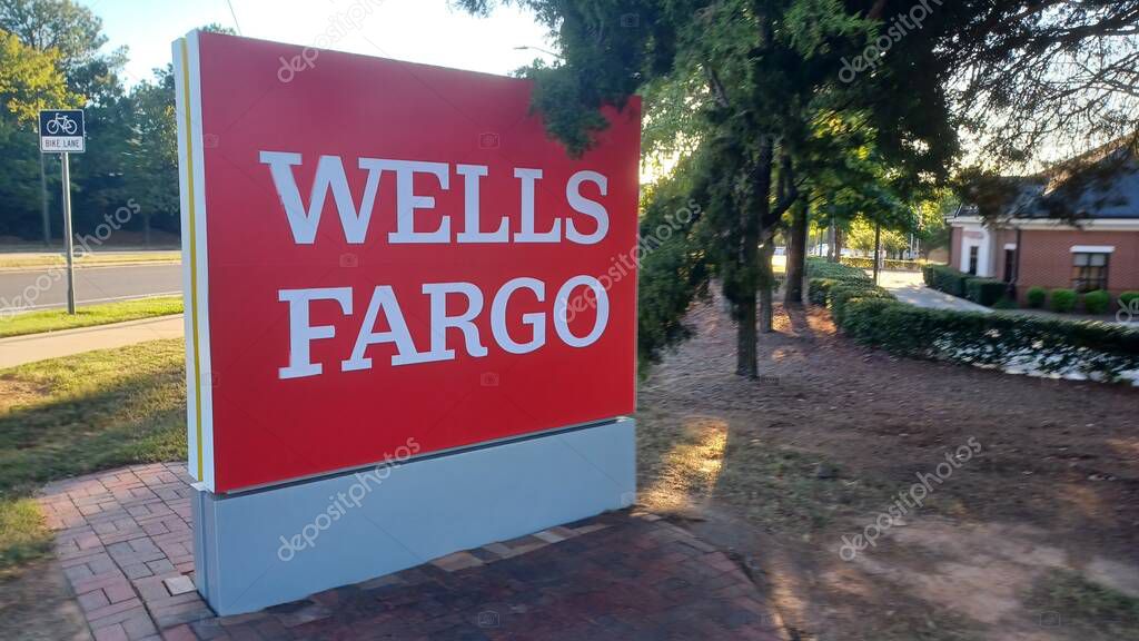 Charlotte, NC, USA - October 10, 2025: Large red Wells Fargo sign stands near a road and trees on a sunny autumn afternoon