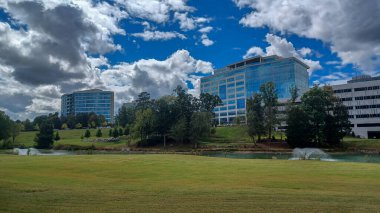 Modern office buildings stand amidst green lawns, trees, and a walking path in Ballantyne Corporate Park under a cloudy sky.