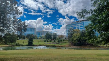 Modern office buildings stand amidst green lawns, trees, and a walking path in Ballantyne Corporate Park under a cloudy sky.