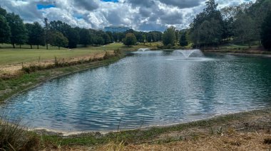 Modern office buildings stand amidst green lawns, trees, and a walking path in Ballantyne Corporate Park under a cloudy sky.