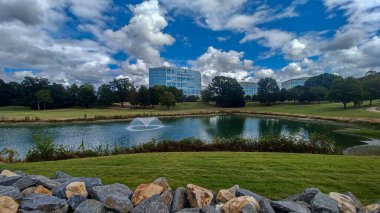 Modern office buildings stand amidst green lawns, trees, and a walking path in Ballantyne Corporate Park under a cloudy sky.