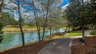 Modern office buildings stand amidst green lawns, trees, and a walking path in Ballantyne Corporate Park under a cloudy sky.
