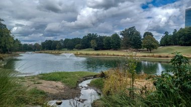 Modern office buildings stand amidst green lawns, trees, and a walking path in Ballantyne Corporate Park under a cloudy sky.