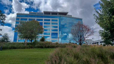 Modern office buildings stand amidst green lawns, trees, and a walking path in Ballantyne Corporate Park under a cloudy sky.