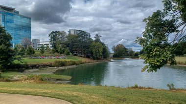 Modern office buildings stand amidst green lawns, trees, and a walking path in Ballantyne Corporate Park under a cloudy sky.