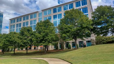 Modern office buildings stand amidst green lawns, trees, and a walking path in Ballantyne Corporate Park under a cloudy sky.