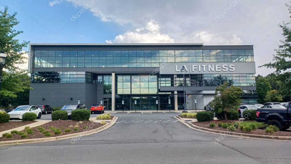 Charlotte, NC, USA - October 2, 2025: The modern glass exterior of an LA Fitness gym building features large letters and parked cars in the foreground.