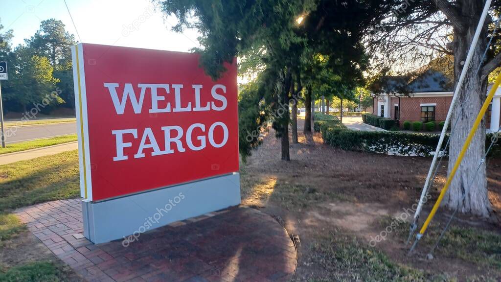 Charlotte, NC, USA - October 10, 2025: Large red Wells Fargo sign stands near a road and trees on a sunny autumn afternoon