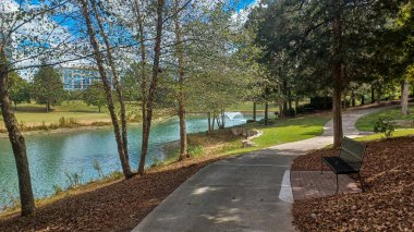 Modern office buildings stand amidst green lawns, trees, and a walking path in Ballantyne Corporate Park under a cloudy sky.