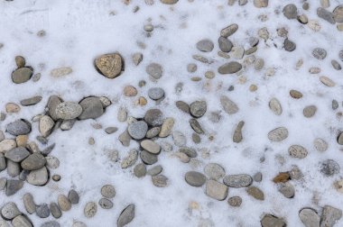 Küçük ve büyük kayalar, kısmen ince bir beyaz kar tabakasıyla kaplı, karlı zemine saçılmış..