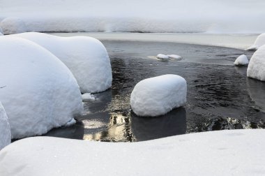 Yoğun karla kaplı büyük kayalar akan bir derede oturur ve yumuşak, yuvarlak şekilli eşsiz bir kış manzarası yaratır..