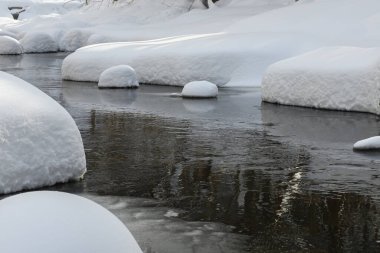 Yoğun karla kaplı büyük kayalar akan bir derede oturur ve yumuşak, yuvarlak şekilli eşsiz bir kış manzarası yaratır..
