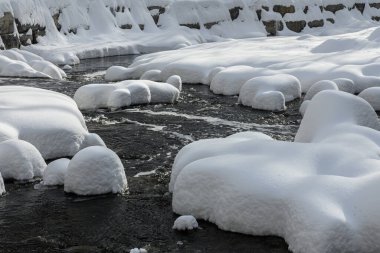 Yoğun karla kaplı büyük kayalar akan bir derede oturur ve yumuşak, yuvarlak şekilli eşsiz bir kış manzarası yaratır..
