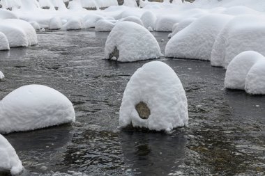 Yoğun karla kaplı büyük kayalar akan bir derede oturur ve yumuşak, yuvarlak şekilli eşsiz bir kış manzarası yaratır..