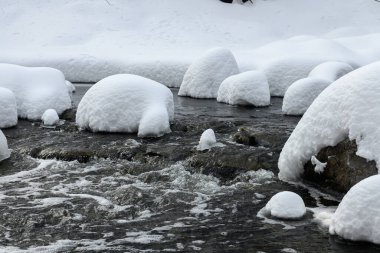 Yoğun karla kaplı büyük kayalar akan bir derede oturur ve yumuşak, yuvarlak şekilli eşsiz bir kış manzarası yaratır..
