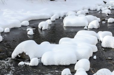 Yoğun karla kaplı büyük kayalar akan bir derede oturur ve yumuşak, yuvarlak şekilli eşsiz bir kış manzarası yaratır..