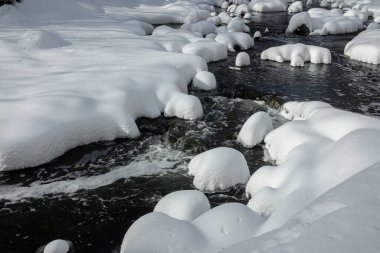 Yoğun karla kaplı büyük kayalar akan bir derede oturur ve yumuşak, yuvarlak şekilli eşsiz bir kış manzarası yaratır..