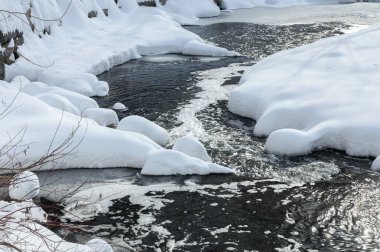 Yoğun karla kaplı büyük kayalar akan bir derede oturur ve yumuşak, yuvarlak şekilli eşsiz bir kış manzarası yaratır..