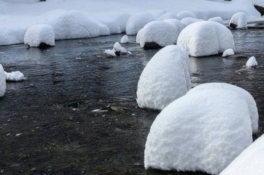 Yoğun karla kaplı büyük kayalar akan bir derede oturur ve yumuşak, yuvarlak şekilli eşsiz bir kış manzarası yaratır..