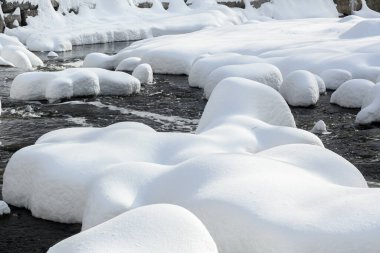 Yoğun karla kaplı büyük kayalar akan bir derede oturur ve yumuşak, yuvarlak şekilli eşsiz bir kış manzarası yaratır..