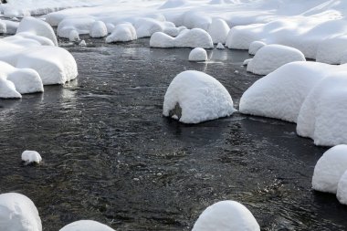 Yoğun karla kaplı büyük kayalar akan bir derede oturur ve yumuşak, yuvarlak şekilli eşsiz bir kış manzarası yaratır..