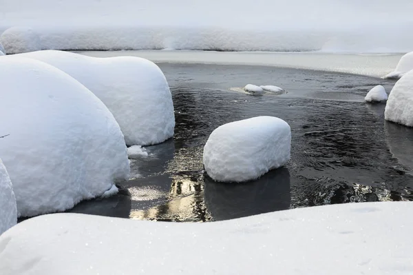 Yoğun karla kaplı büyük kayalar akan bir derede oturur ve yumuşak, yuvarlak şekilli eşsiz bir kış manzarası yaratır..