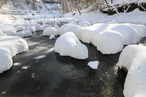 Yoğun karla kaplı büyük kayalar akan bir derede oturur ve yumuşak, yuvarlak şekilli eşsiz bir kış manzarası yaratır..