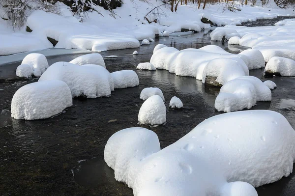 Yoğun karla kaplı büyük kayalar akan bir derede oturur ve yumuşak, yuvarlak şekilli eşsiz bir kış manzarası yaratır..