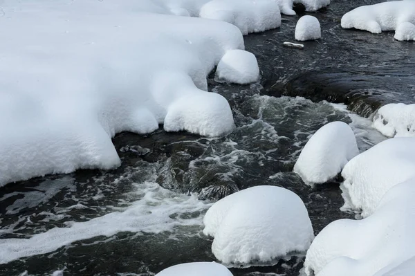 Yoğun karla kaplı büyük kayalar akan bir derede oturur ve yumuşak, yuvarlak şekilli eşsiz bir kış manzarası yaratır..