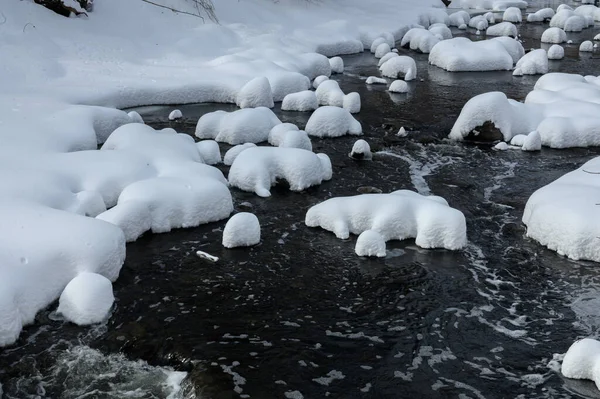 Yoğun karla kaplı büyük kayalar akan bir derede oturur ve yumuşak, yuvarlak şekilli eşsiz bir kış manzarası yaratır..