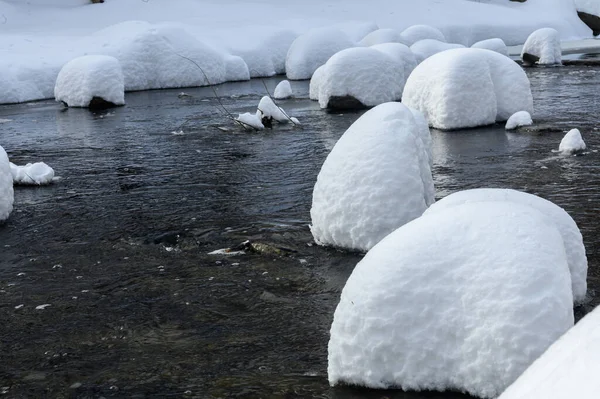 Yoğun karla kaplı büyük kayalar akan bir derede oturur ve yumuşak, yuvarlak şekilli eşsiz bir kış manzarası yaratır..