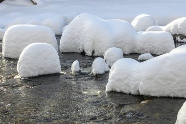 Yoğun karla kaplı büyük kayalar akan bir derede oturur ve yumuşak, yuvarlak şekilli eşsiz bir kış manzarası yaratır..