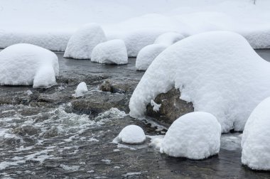 Yoğun karla kaplı büyük kayalar akan bir derede oturur ve yumuşak, yuvarlak şekilli eşsiz bir kış manzarası yaratır..
