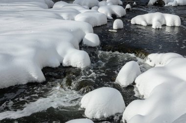 Yoğun karla kaplı büyük kayalar akan bir derede oturur ve yumuşak, yuvarlak şekilli eşsiz bir kış manzarası yaratır..