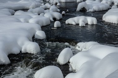 Yoğun karla kaplı büyük kayalar akan bir derede oturur ve yumuşak, yuvarlak şekilli eşsiz bir kış manzarası yaratır..