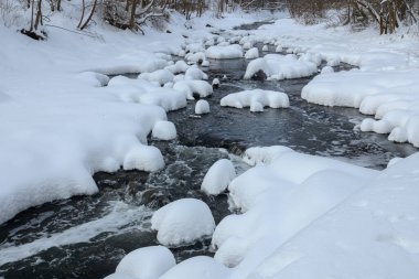 Yoğun karla kaplı büyük kayalar akan bir derede oturur ve yumuşak, yuvarlak şekilli eşsiz bir kış manzarası yaratır..